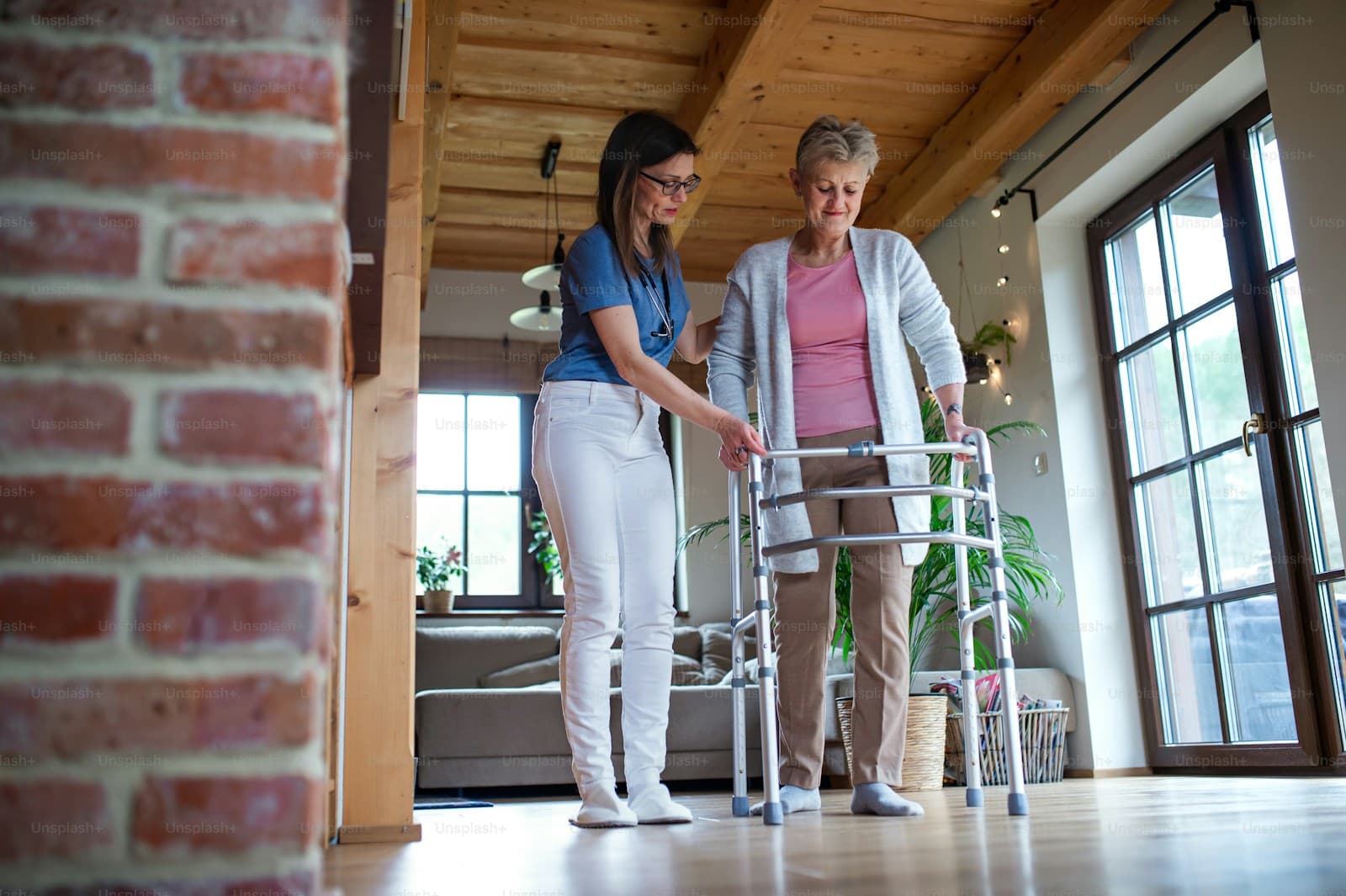 A physiotherapist helping a senior patient with a walker at home in Surat
